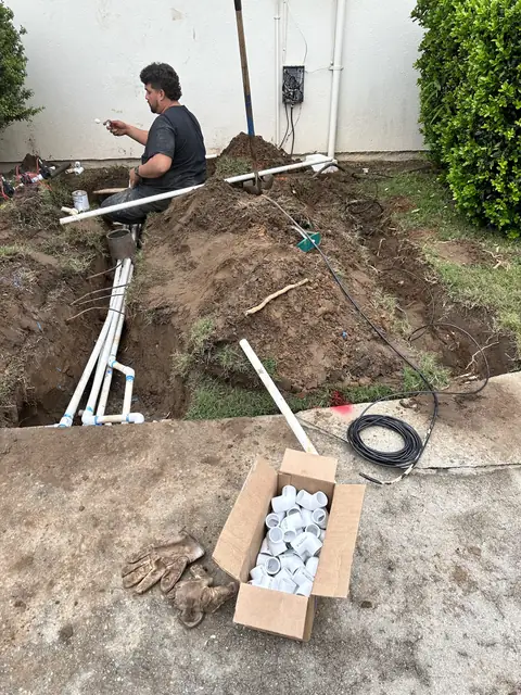 White PVC irrigation manifold being assembled in an open trench beside a box of fittings